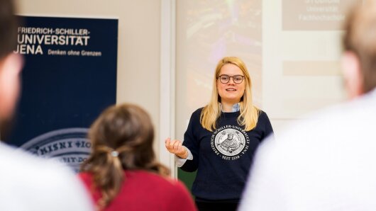 Infomobil: eine Mitarbeiterin der Uni Jena hält einen Vortrag vor einer Schulklasse.